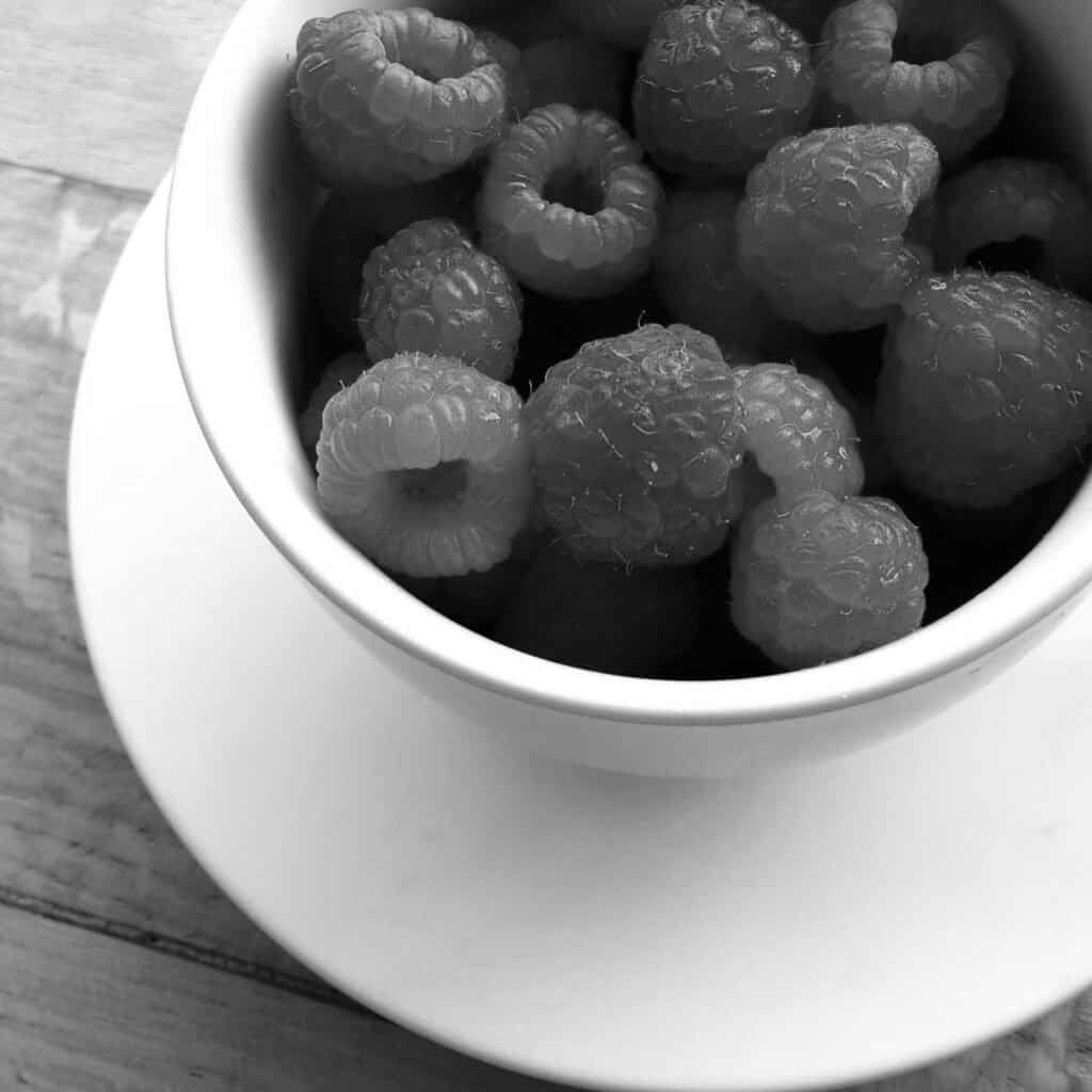 Framboises fraîches dans un bol blanc, en noir et blanc.
